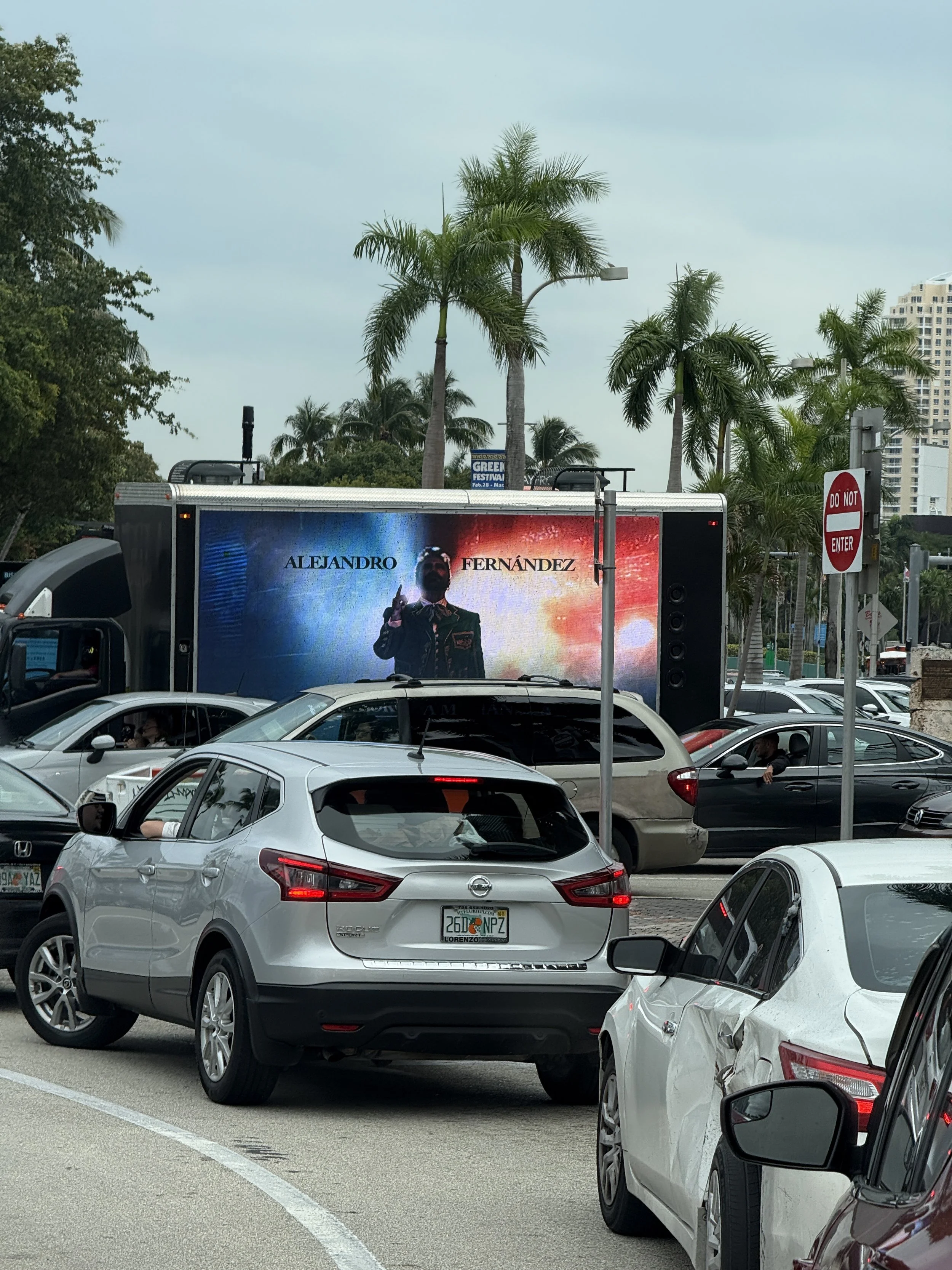 Digital LED billboard truck showing a concert promotion in traffic on a palm-lined street