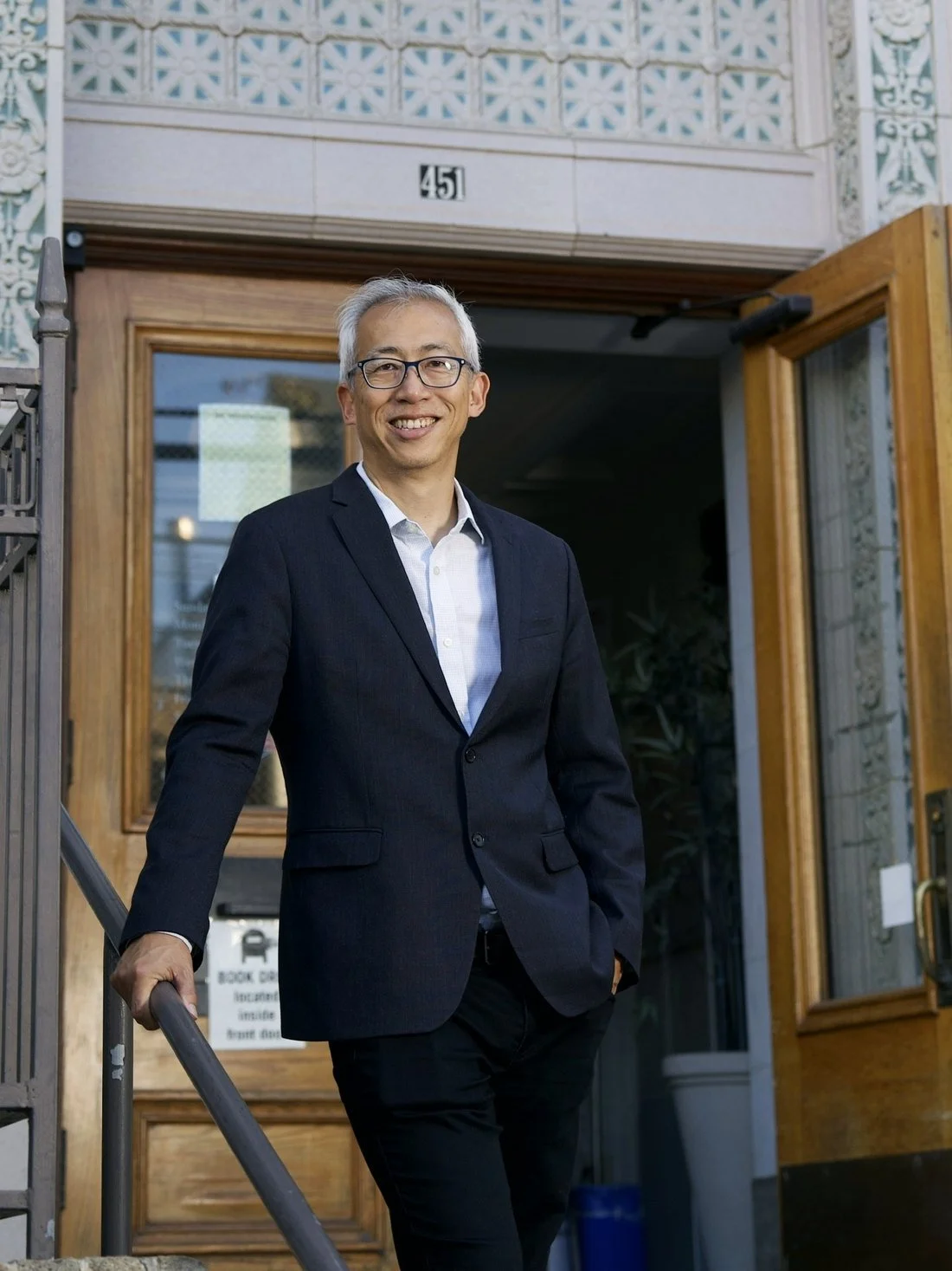 Laurance Lee de pie en la entrada de una biblioteca pública de San Francisco, con la mano en el pasamanos
