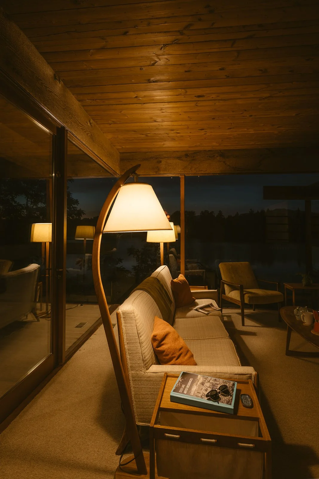 A warm reading lamp and lounge chair in a wood-panelled room at dusk