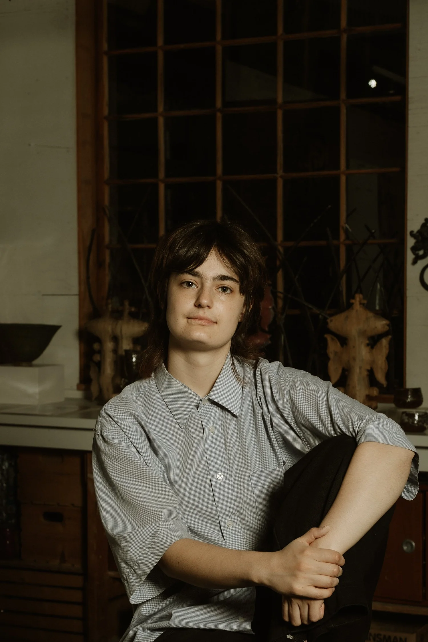 A ceramicist seated in her studio, a grid of window panes behind her