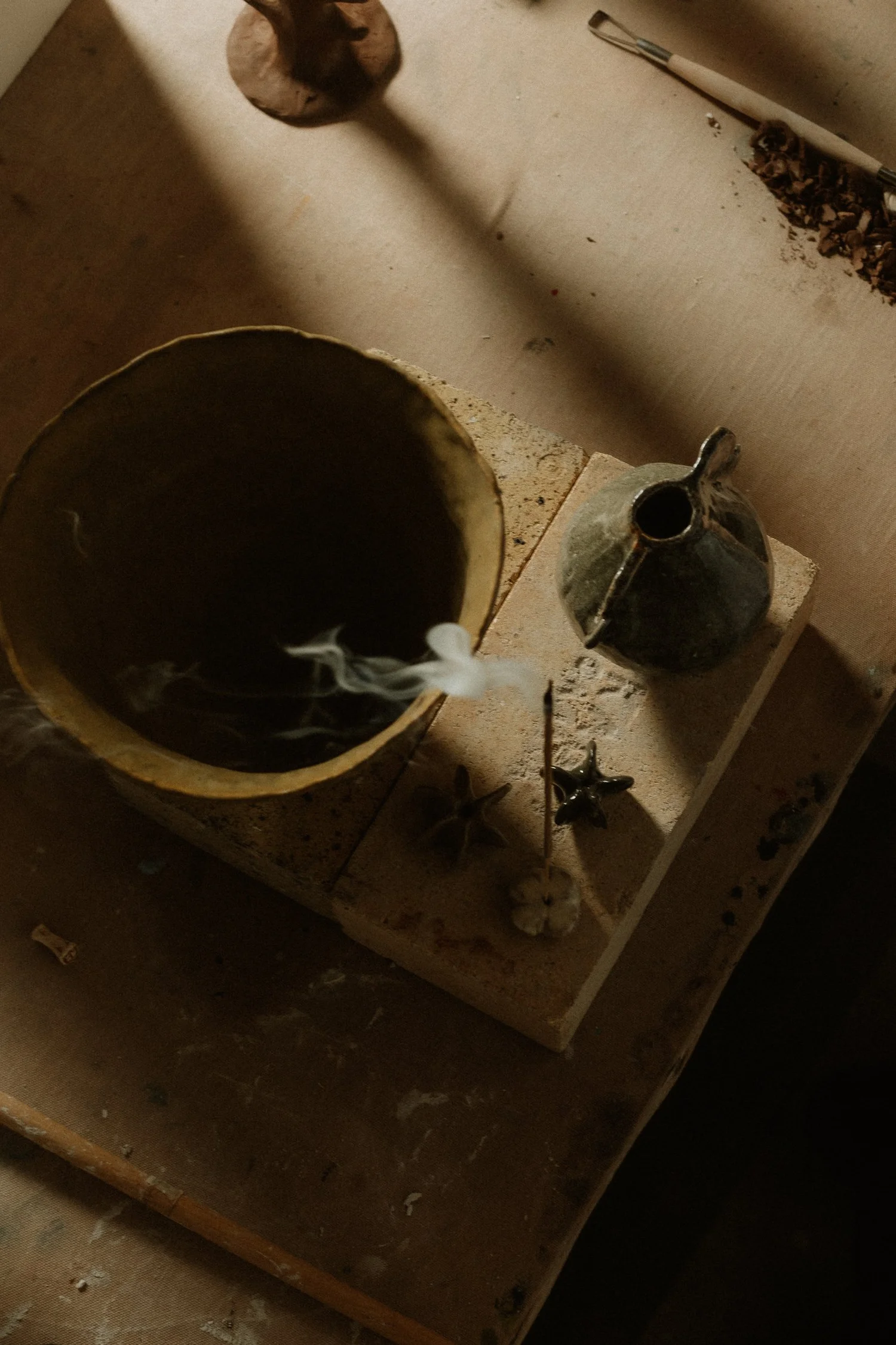 Incense smoke curling from a clay bowl on a studio workbench