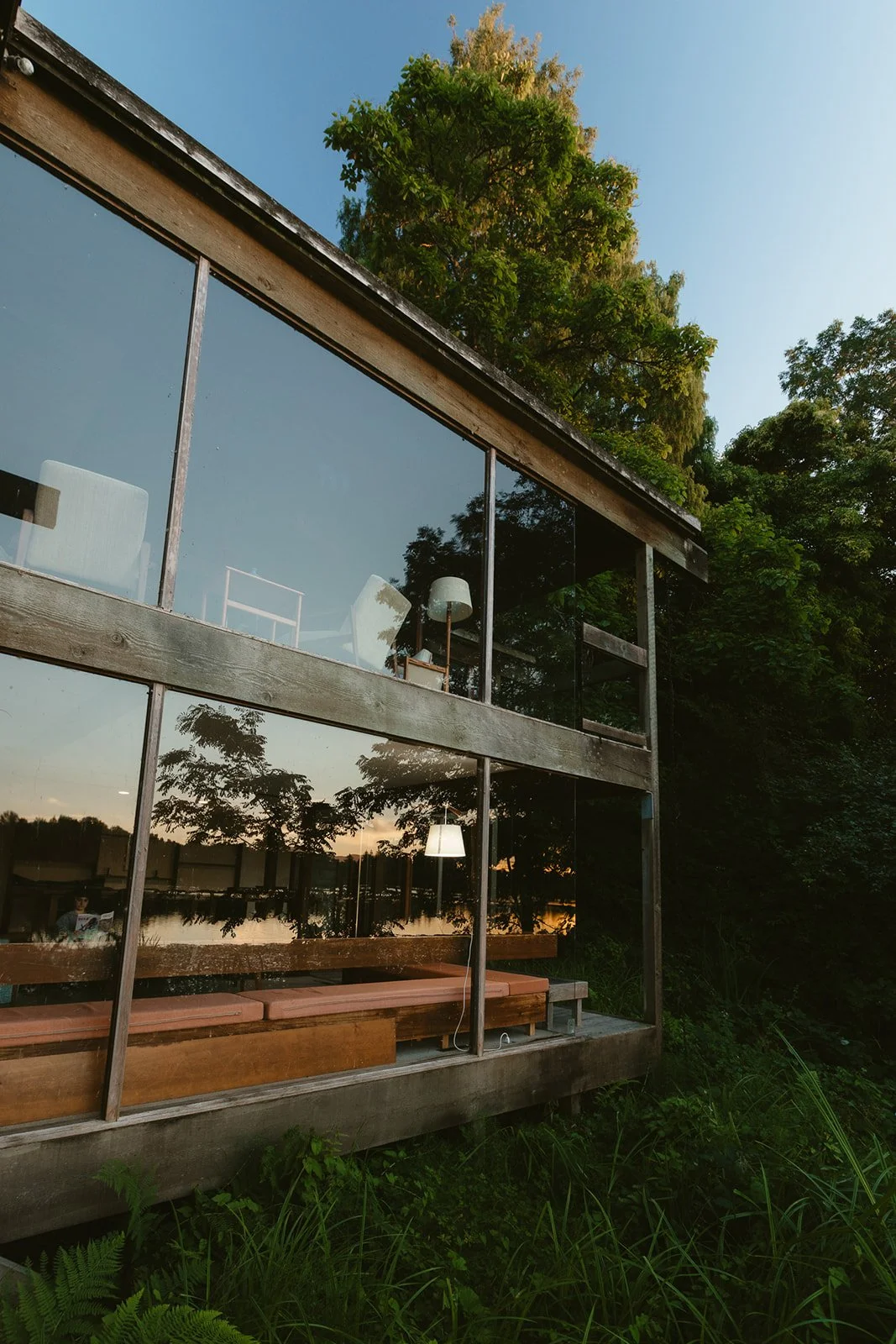 Trees and sky reflected in the glass walls of a modernist house