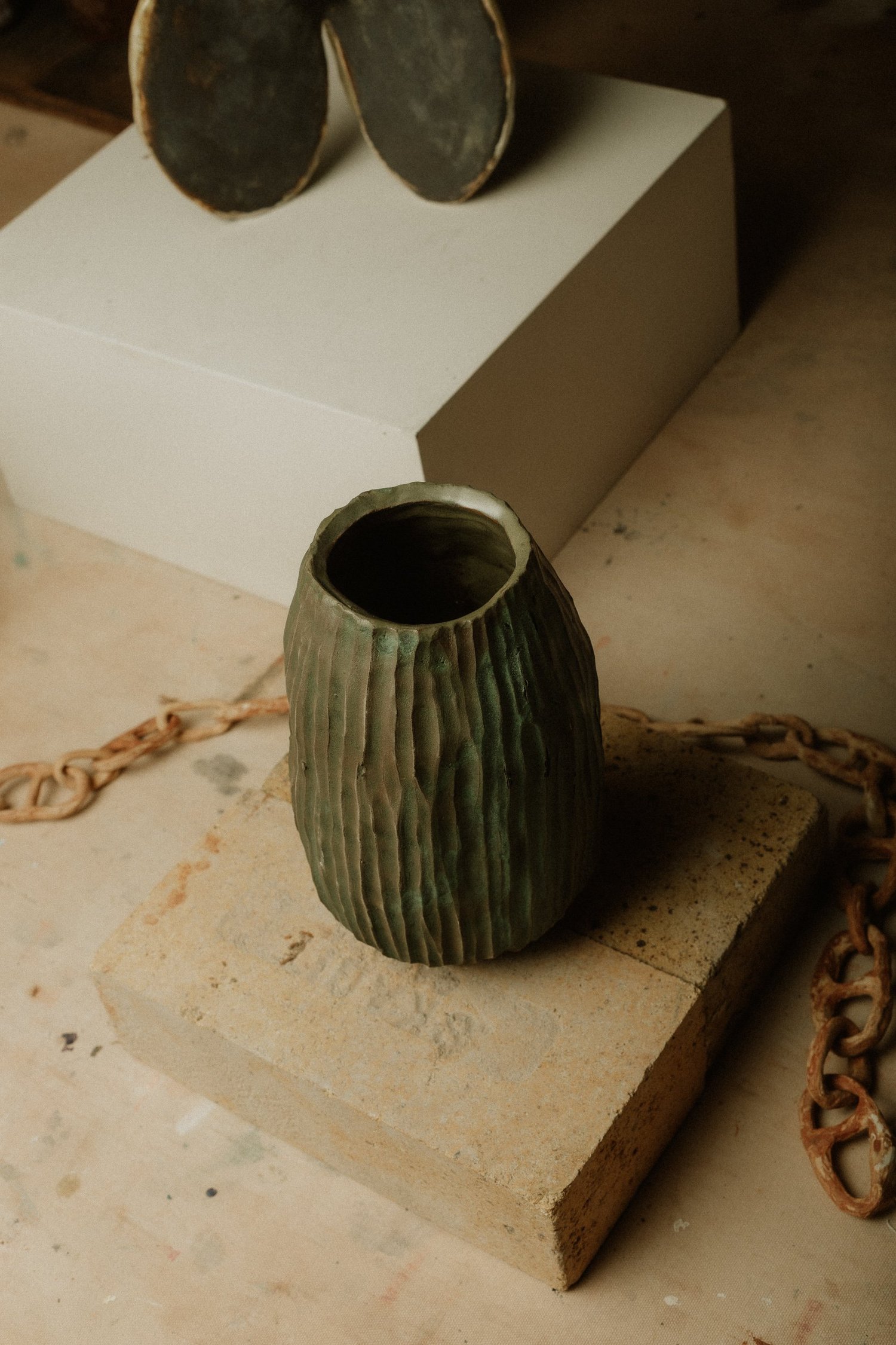 A carved green vessel resting on a pale plinth in soft window light