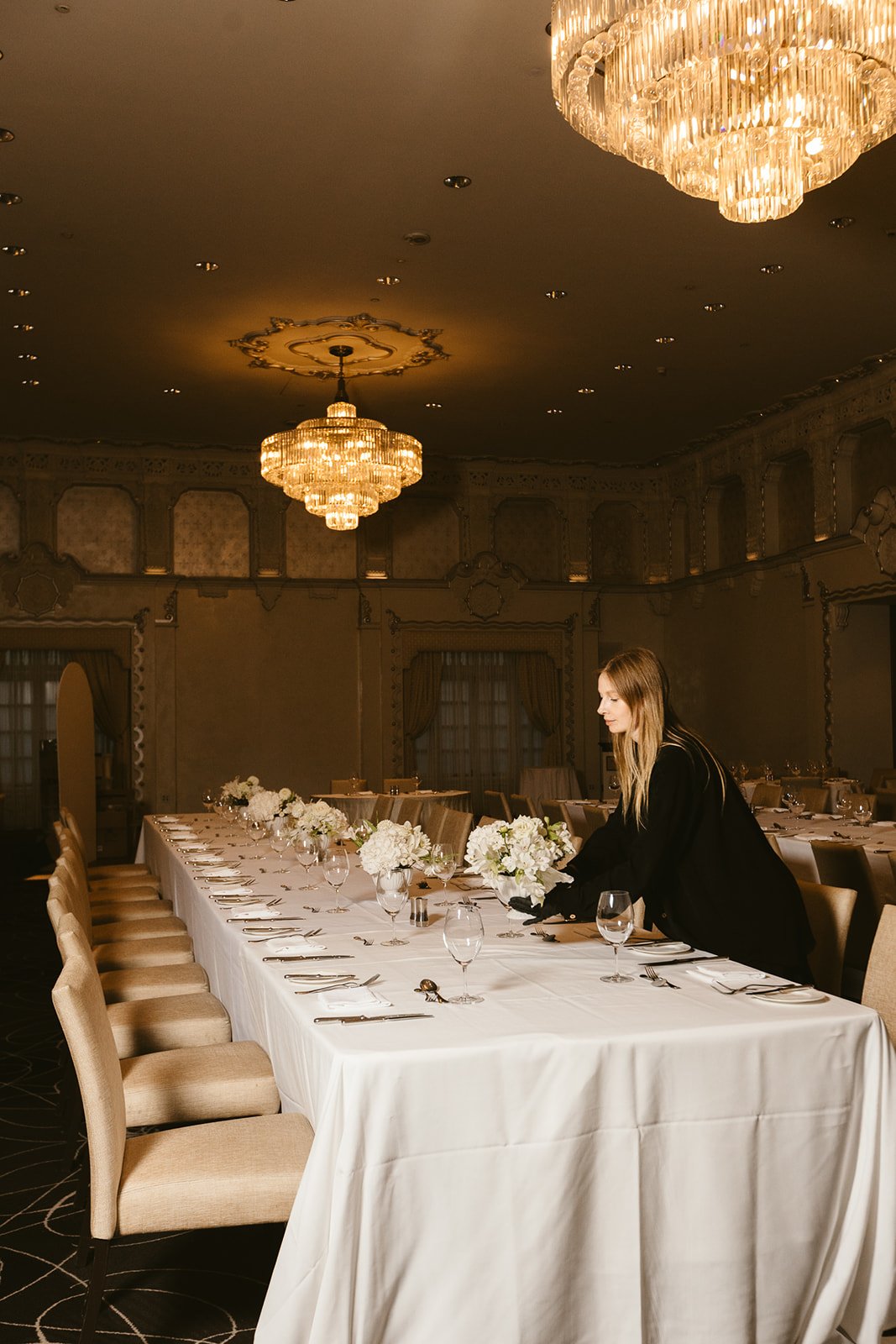A florist arranging flowers at a long table beneath crystal chandeliers