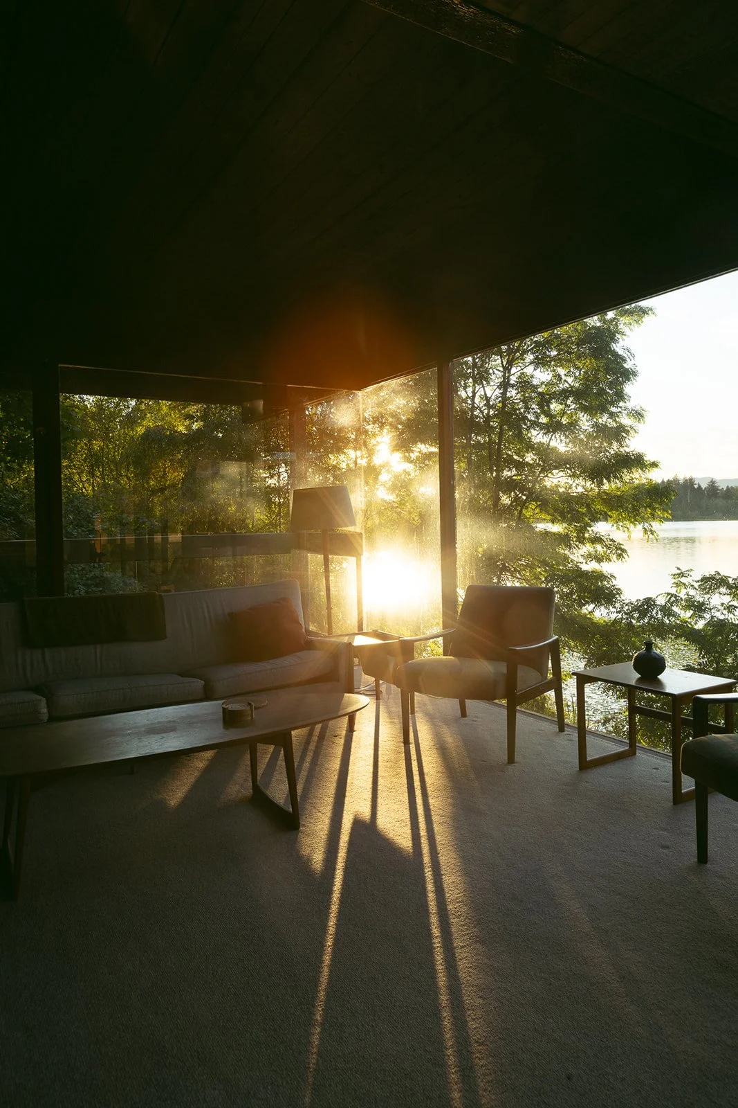 Low sun pouring through floor-to-ceiling glass into a quiet lakeside living room