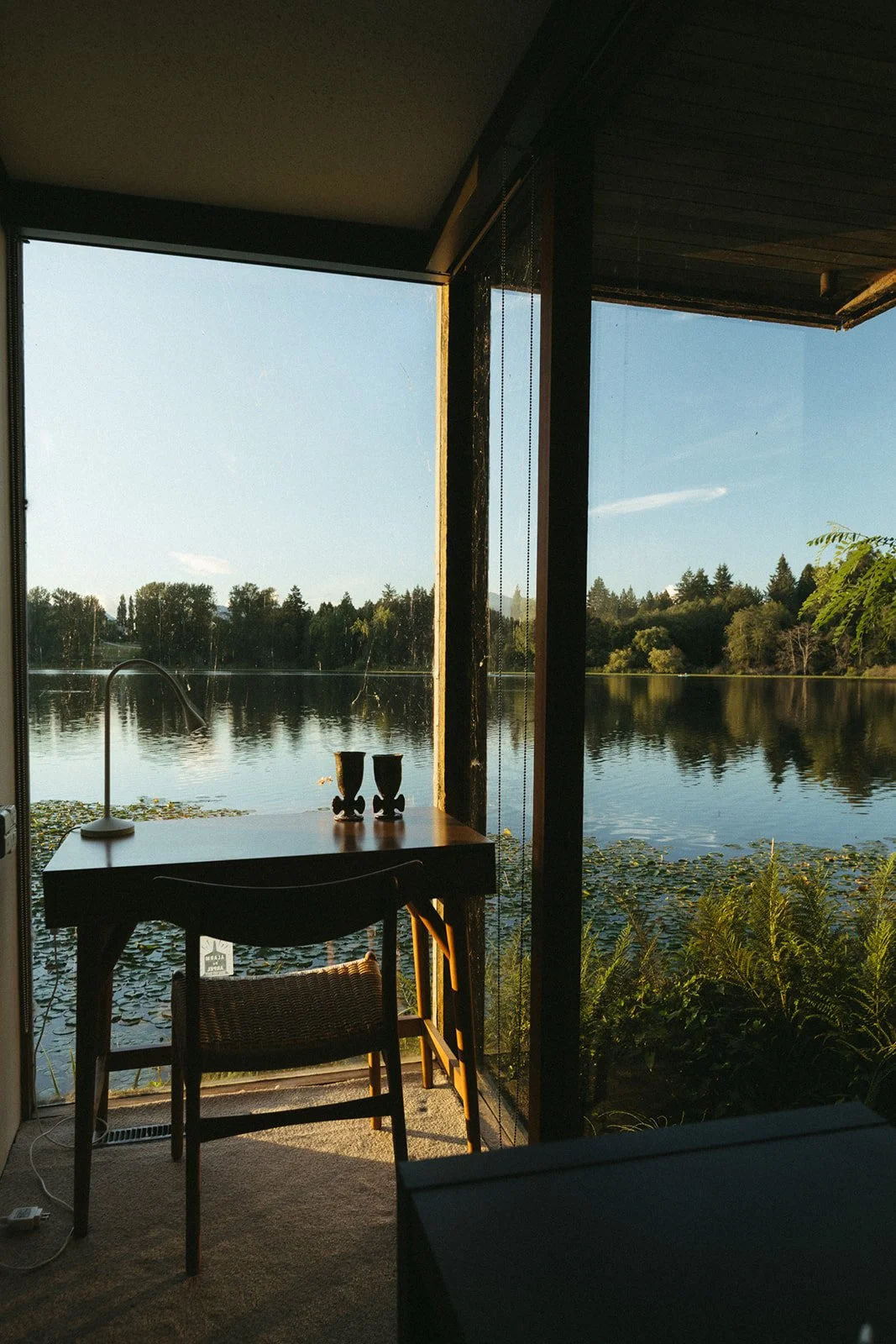 A lake framed by floor-to-ceiling windows and a simple wooden desk