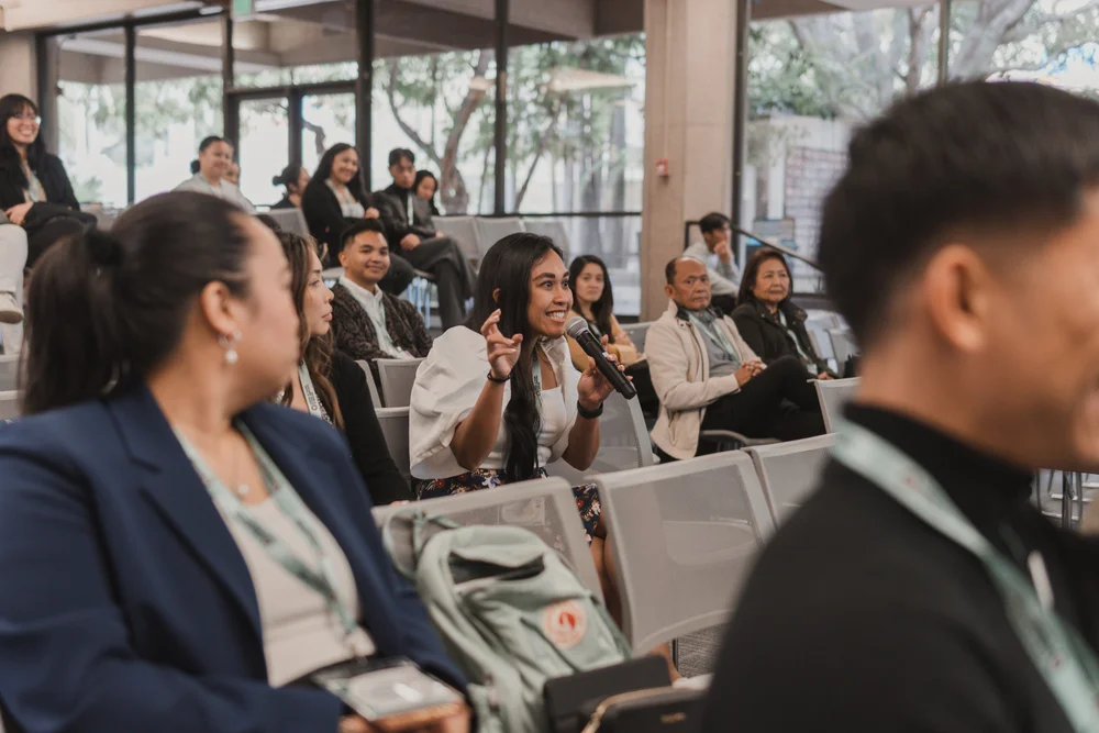 An attendee smiles and asks a question into a microphone during a workshop at a past CYFAM conference.