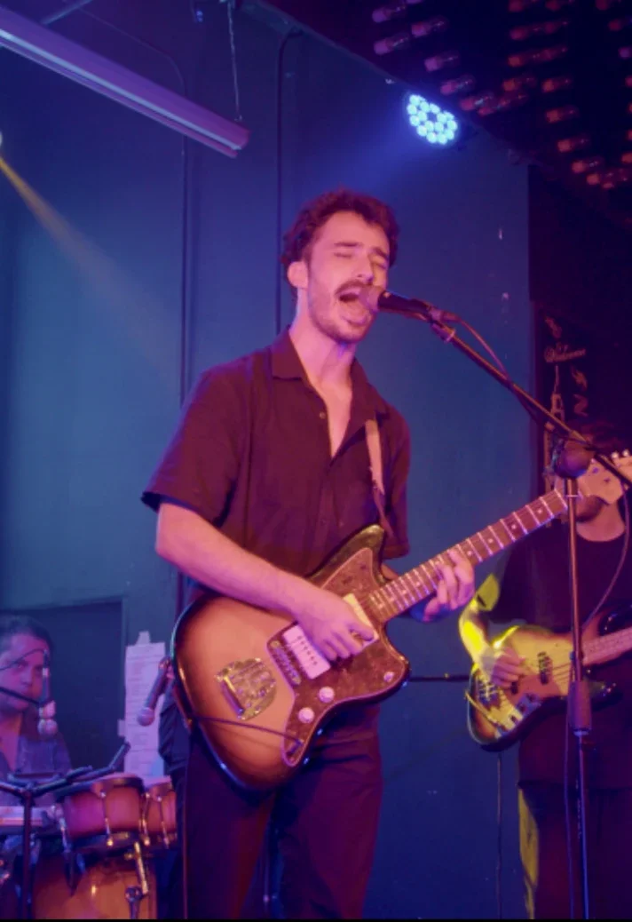 Selvas cantando y tocando guitarra con su banda bajo luces violetas