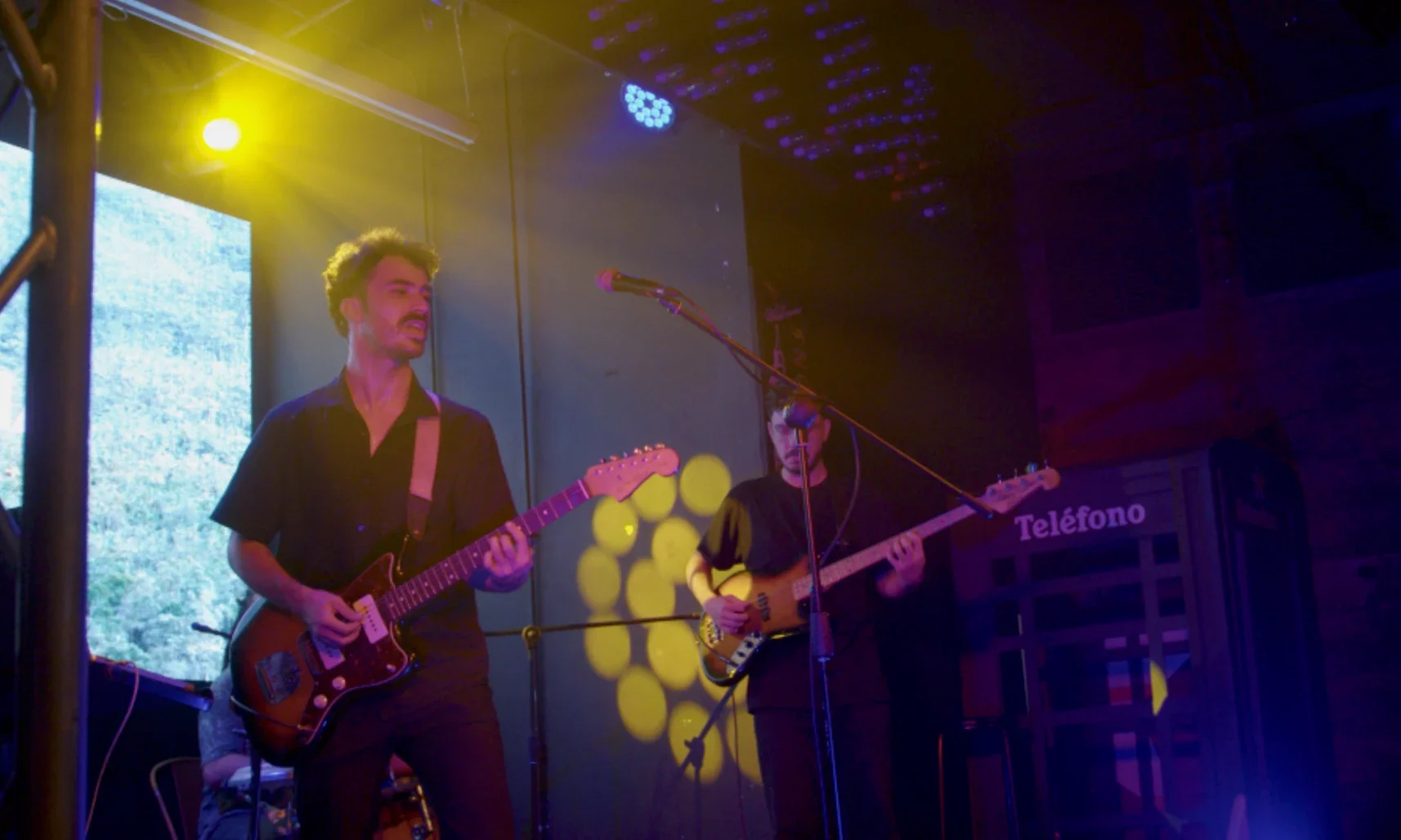 Selvas en concierto con guitarra, voz y bajo bajo luces cálidas