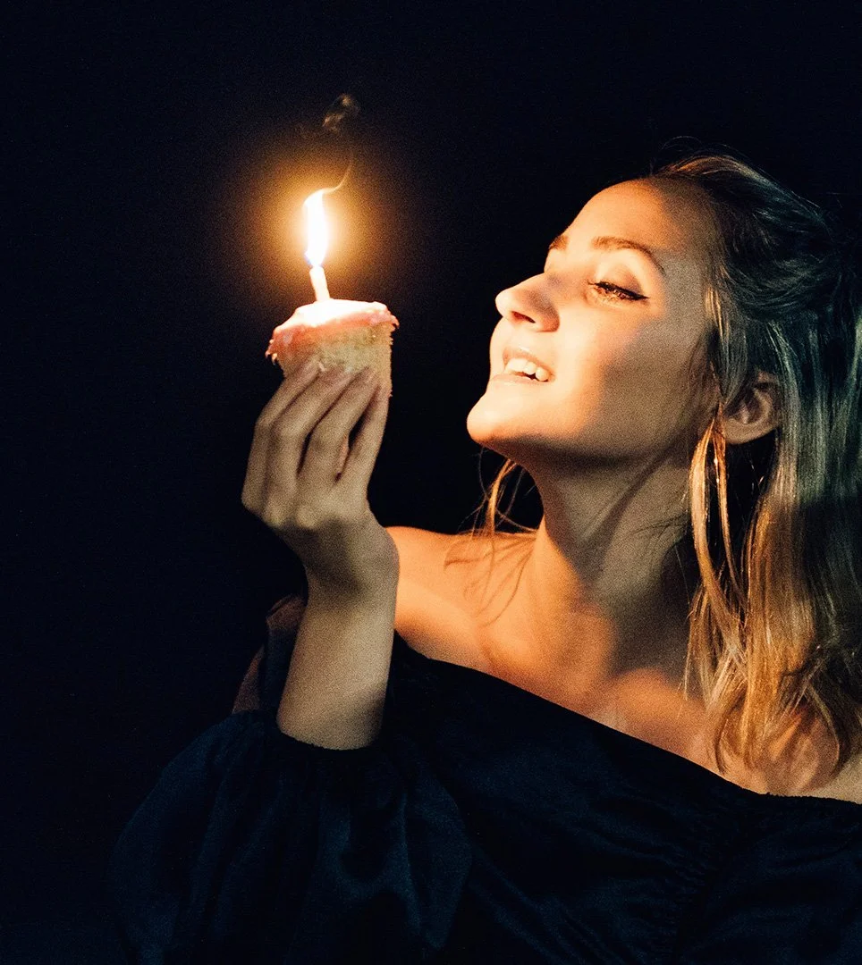 A woman lit by the single candle on her cupcake