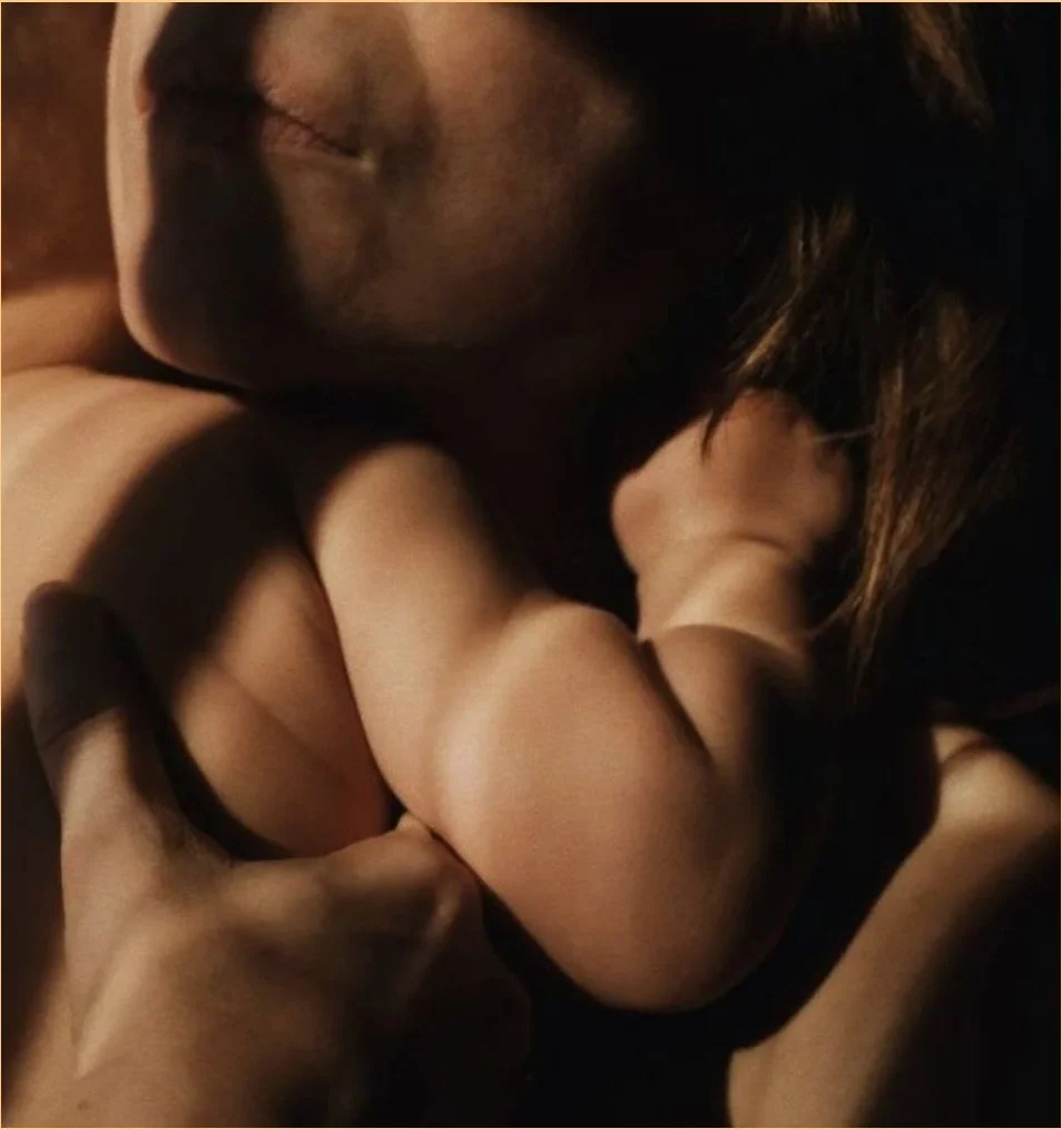 A mother holds her sleeping baby close, in warm low light