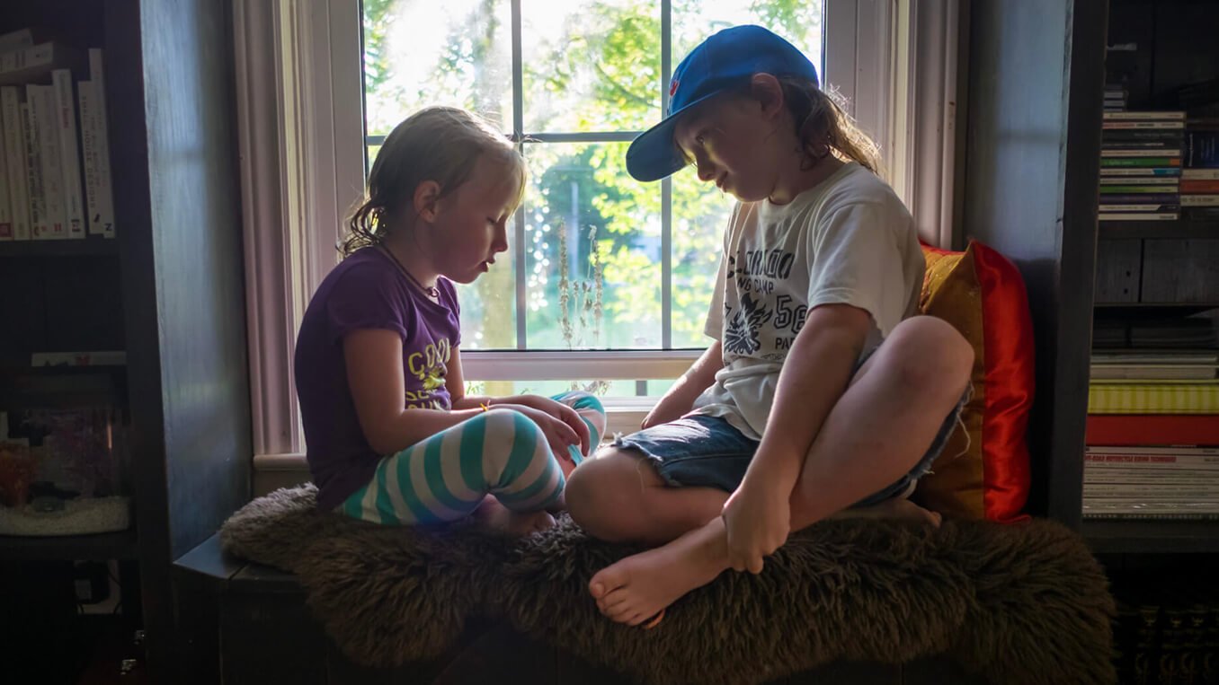 Portrait of a brother and sister sitting in a window.