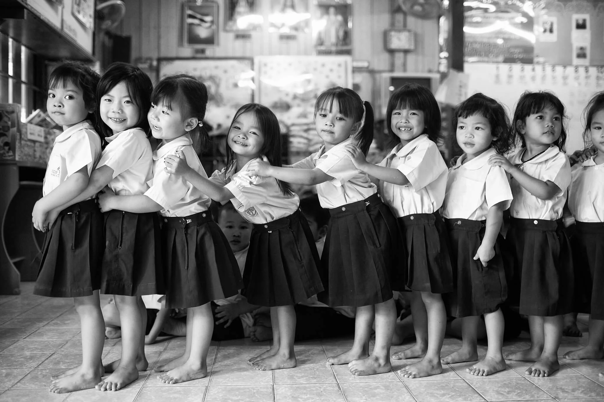 Young school-girls laugh as they line up to go outside to play at lunch, Bangkok. Ian Taylor Photographer.