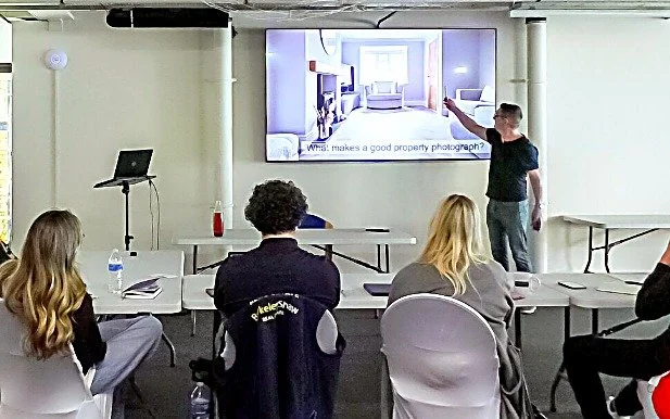 Alex teaching a property photography training session, pointing out framing on screen to a seated group of estate agents