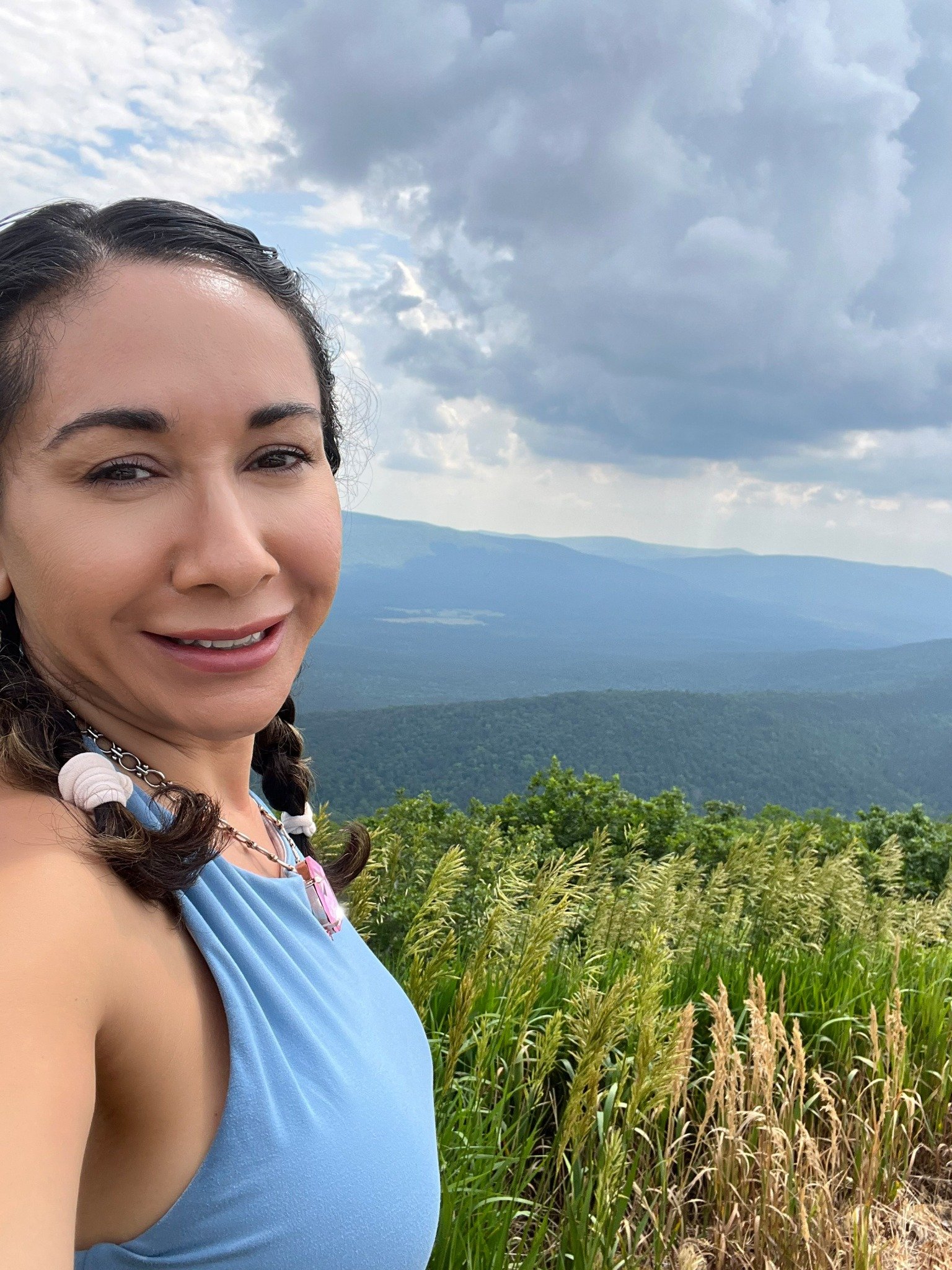 Stephanie in a light blue top with mountains and dramatic clouds behind her