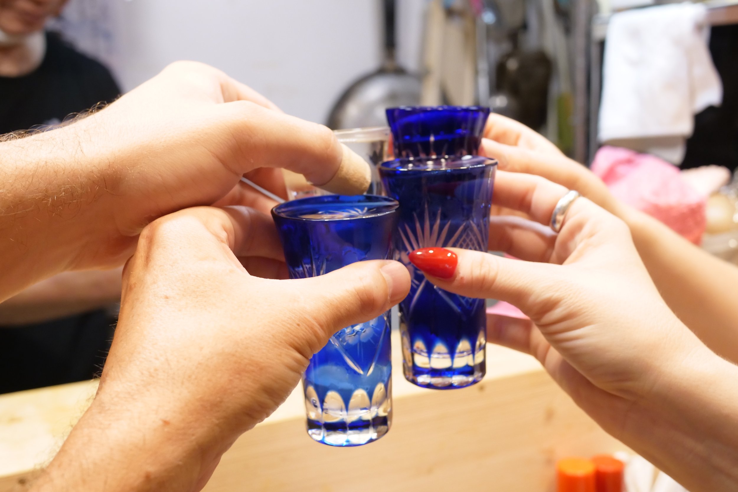 Four blue cut-glass sake cups raised together in a kanpai toast