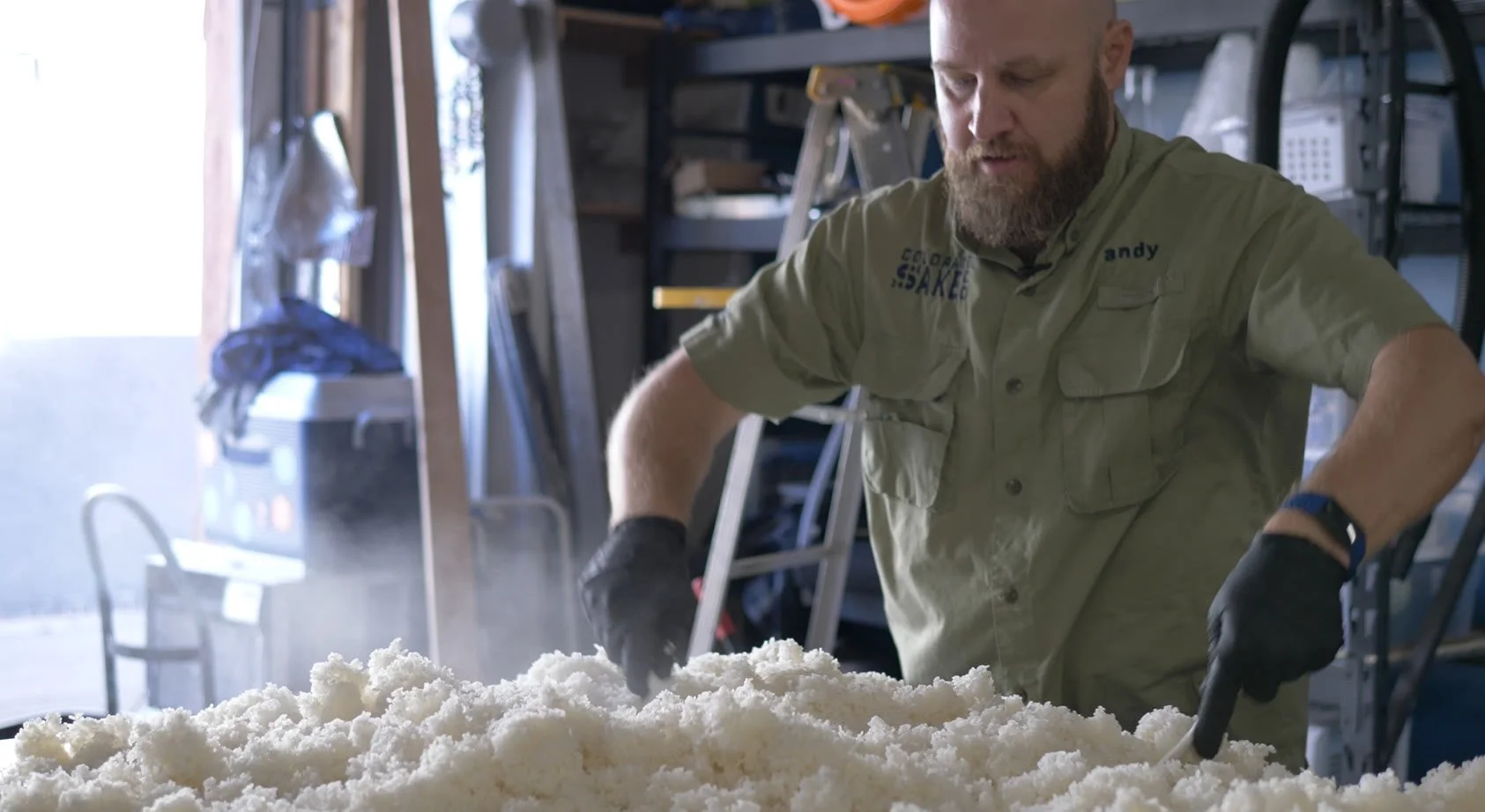 A Colorado Sake Co. brewer spreading and cooling steamed rice by hand