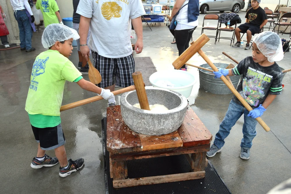 Two young boys pounding mochi rice in a traditional stone mortar (usu) with wooden mallets during a mochitsuki ceremony