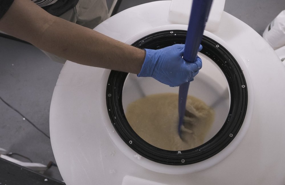 A gloved hand stirring the moromi mash inside a Colorado Sake Co. fermentation tank