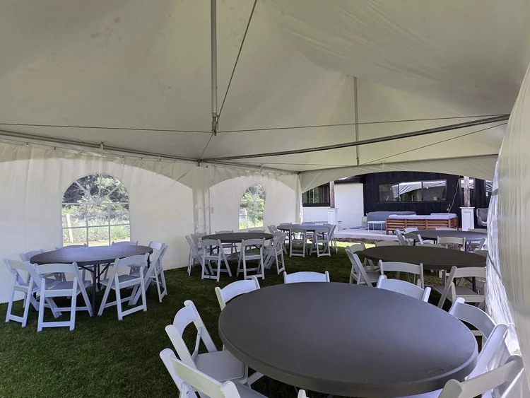 Round tables and white folding chairs inside a marquee tent