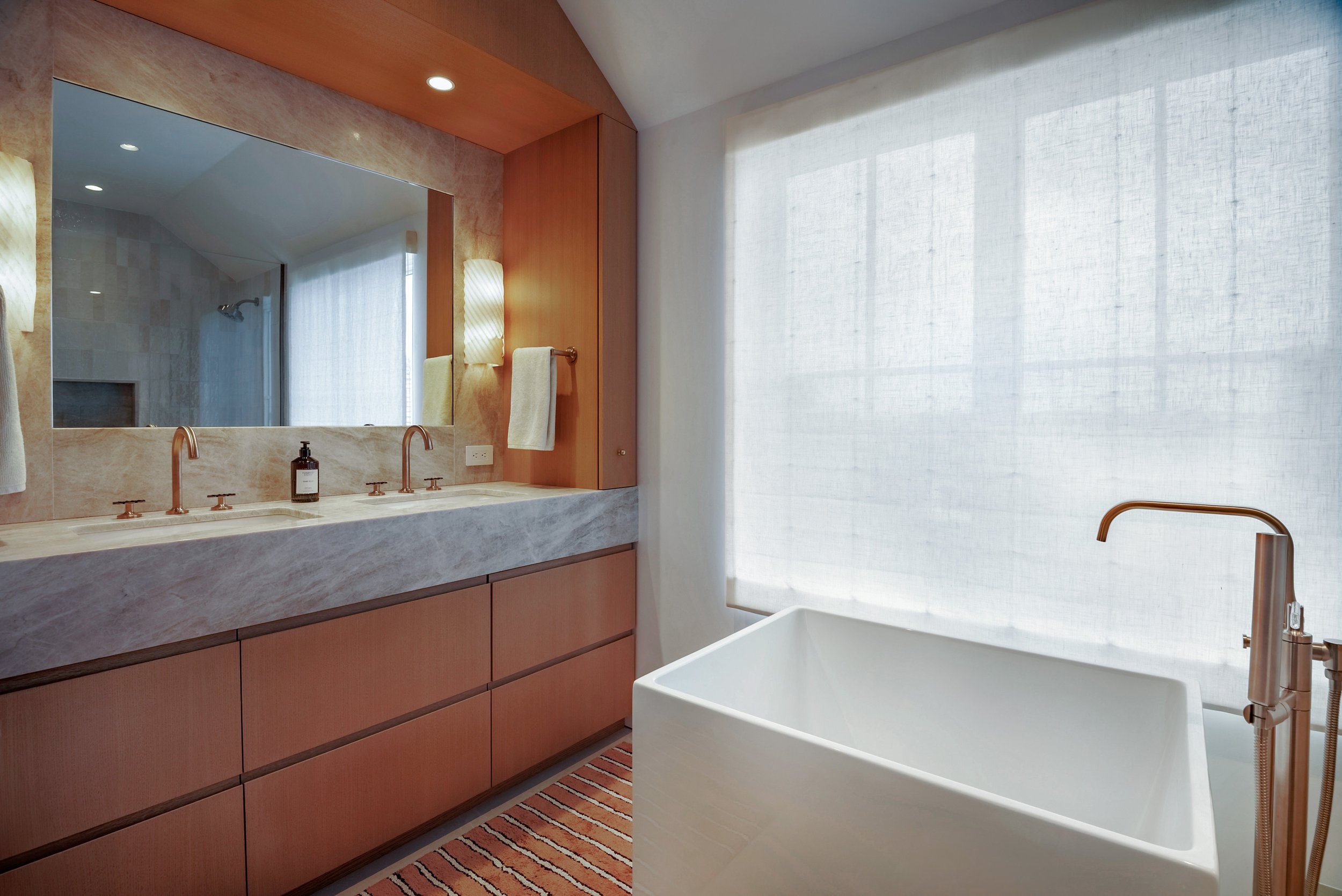Primary bathroom with a long stone double vanity and white oak drawers beside a soaking tub in a Hamptons gut renovation