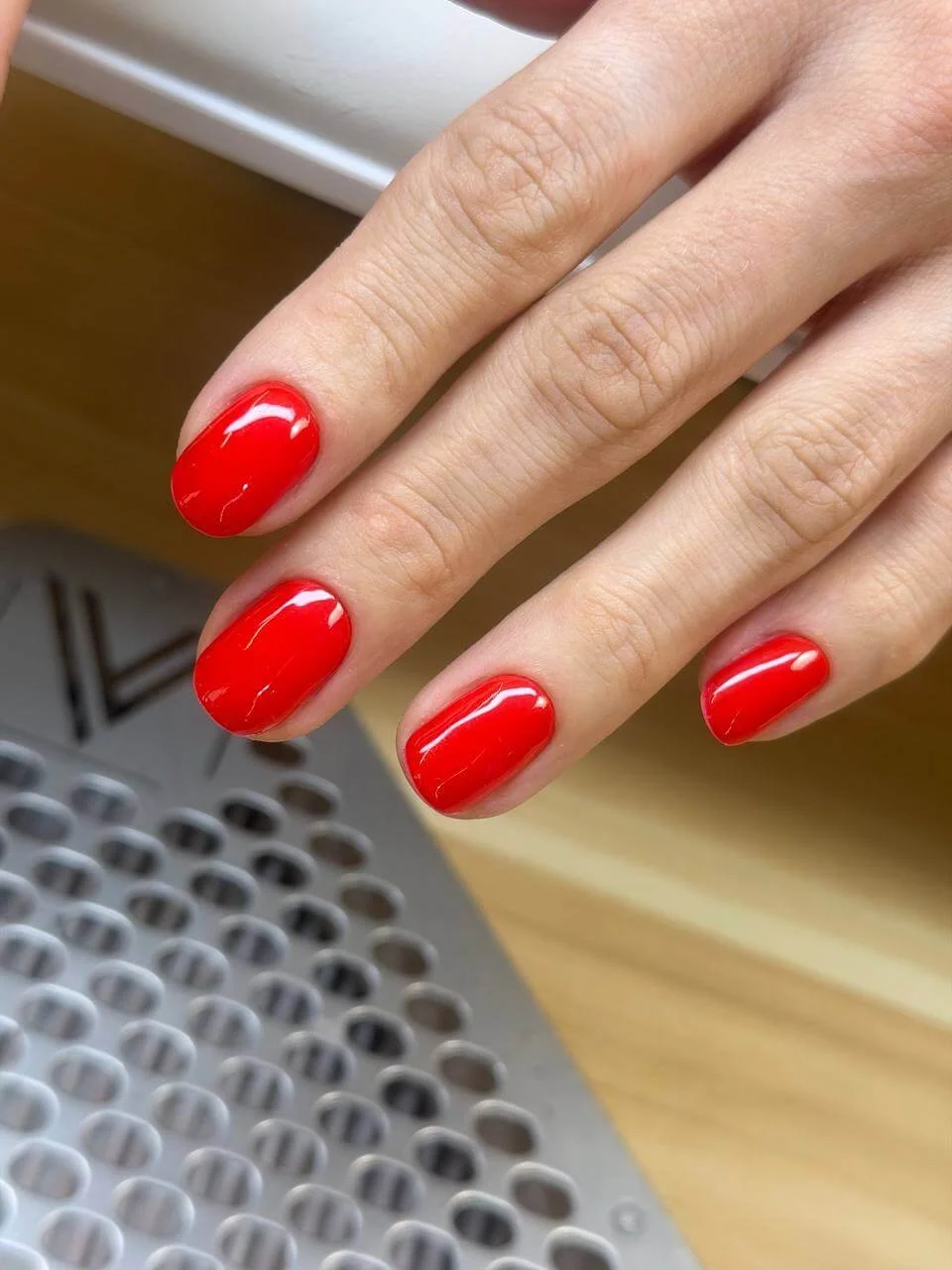 Glossy bright red gel manicure finished in a thin layer over selectively reinforced natural nail tips