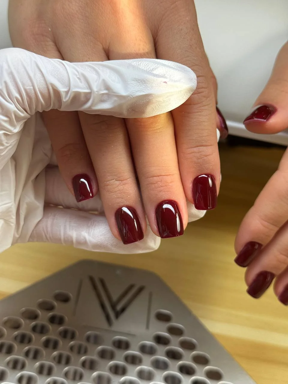 Second view of the finished glossy deep burgundy short manicure held by the nail technician