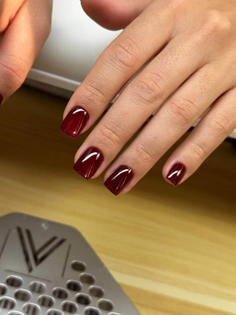 Completed short burgundy soft gel manicure after sidewall reshaping and removal of lifted product