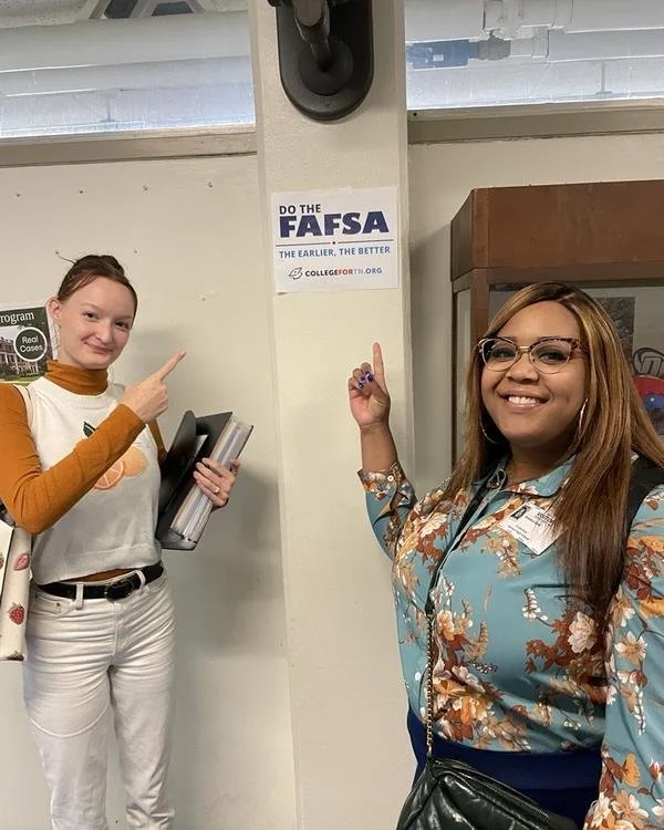 A tnAchieves student and staff member point to a sign encouraging students to do the FAFSA