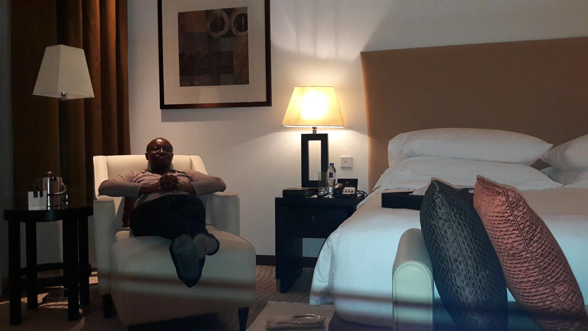 Adult traveller resting in a hotel room after a travel day, reflecting body-aware travel planning, pacing, and recovery.