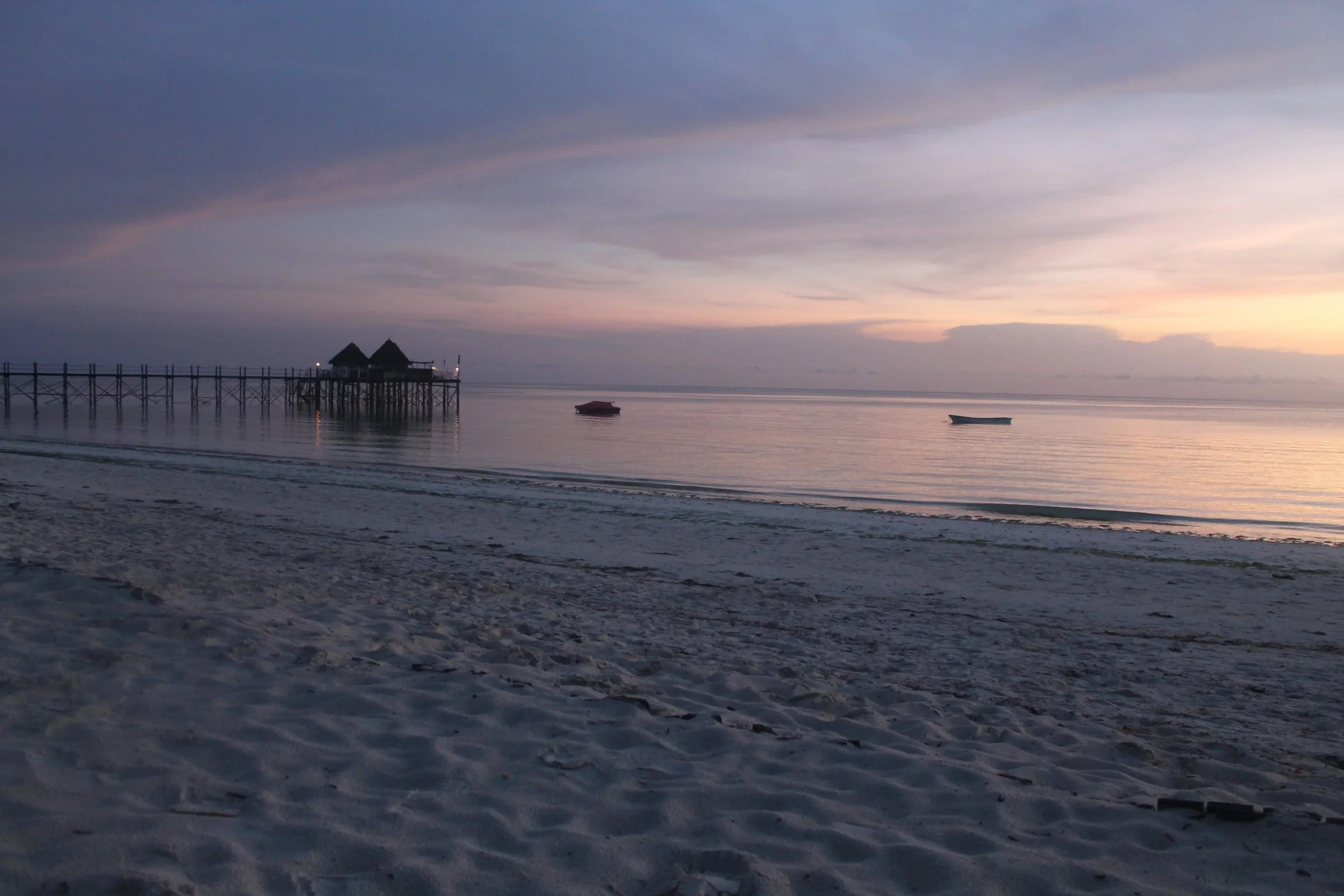 A beach in Zanzibar at dusk, with calm water and warm fading light.