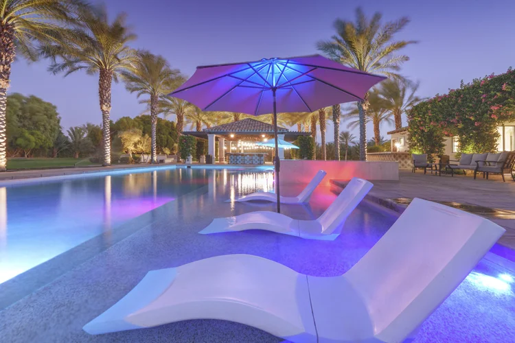 Resort pool at dusk with a glowing umbrella and loungers