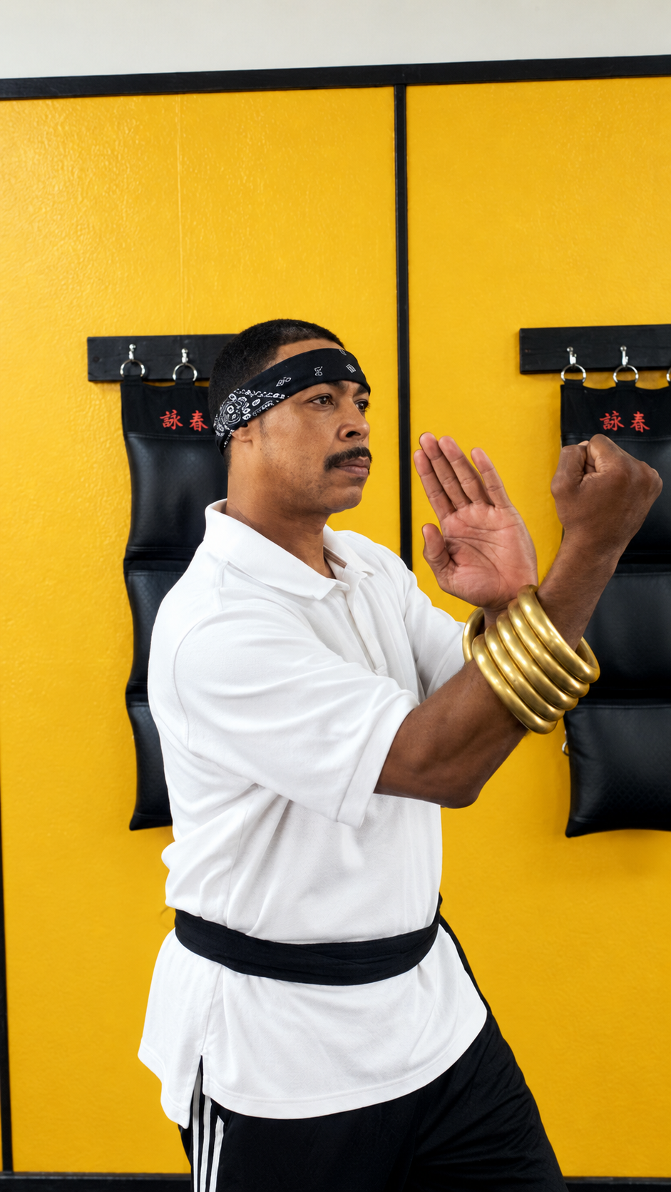 Wing Chun practitioner demonstrates a hand form against the gold dojo wall