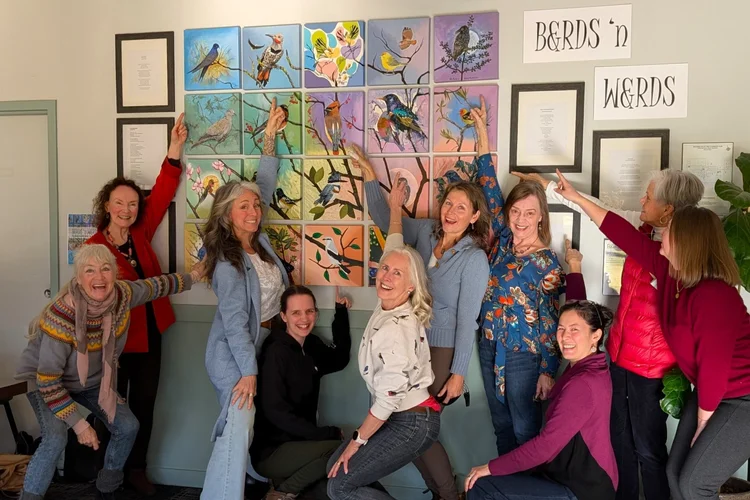 Artists and poets gathering around a collaborative art piece and pointing at their work.