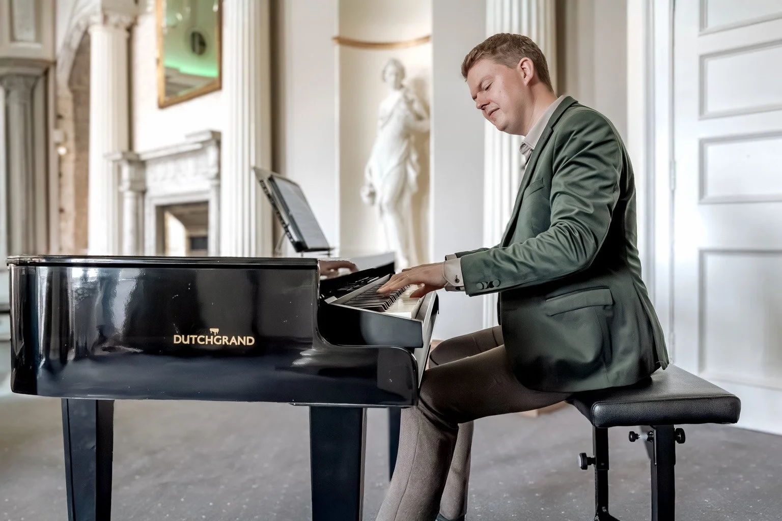 Pianist playing a black baby grand piano in a light, columned wedding venue