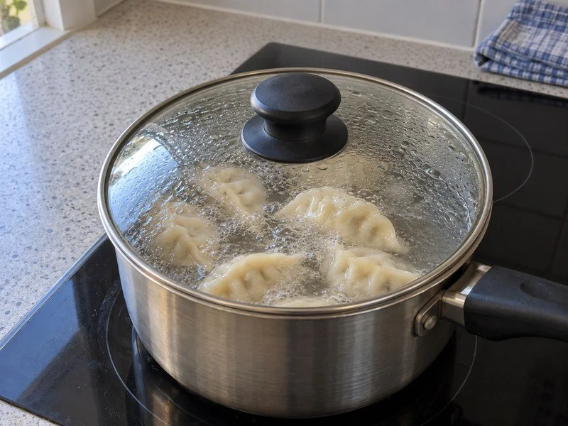 Dumplings simmering in a saucepan under a glass lid. / 饺子在盖着玻璃锅盖的锅中慢煮。