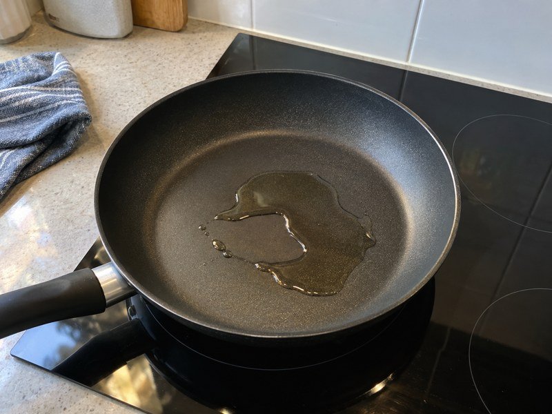 A small amount of oil in a non-stick frying pan on the hob. / 炉灶上的不粘平底锅内放有少量油。