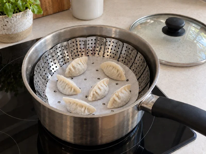 Frozen dumplings spaced apart on the lined steamer rack, ready to cover. / 冷冻饺子间隔摆放在铺好蒸垫的蒸屉上，准备盖上锅盖。