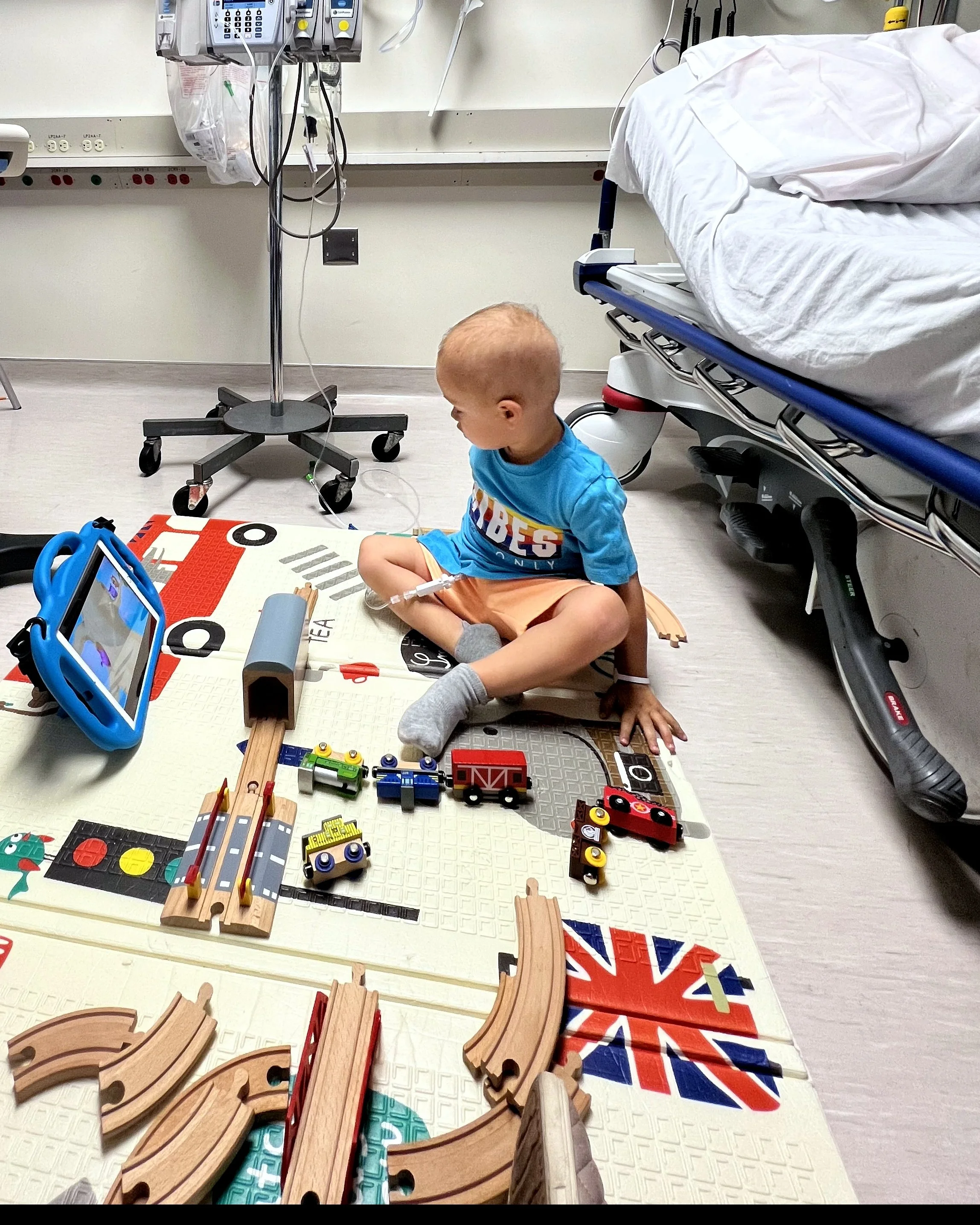 Max, the son of our founder, playing with a wooden train set on the floor of his hospital room during cancer treatment