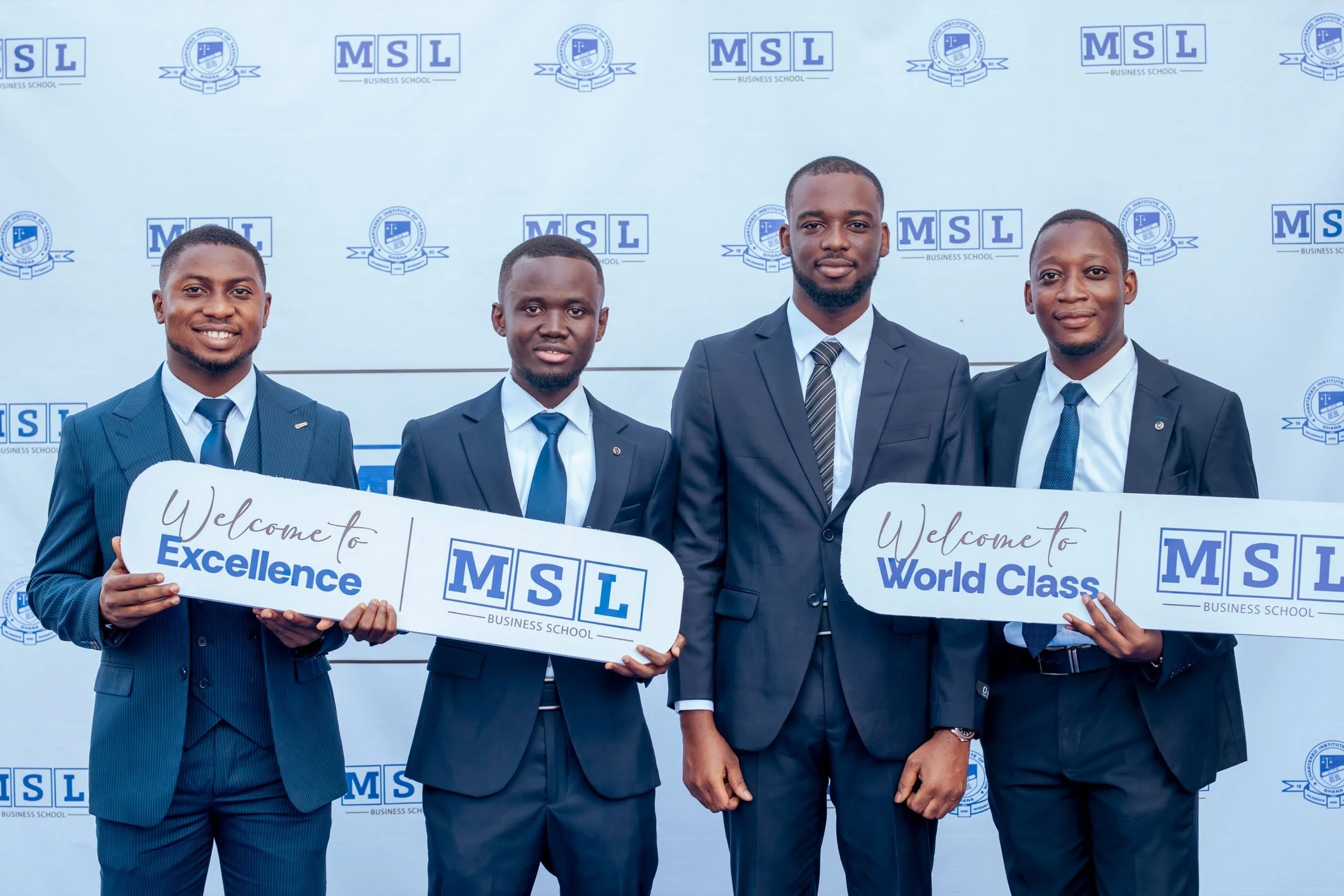 Four smiling MSL students holding Welcome to Excellence and Welcome to World Class placards