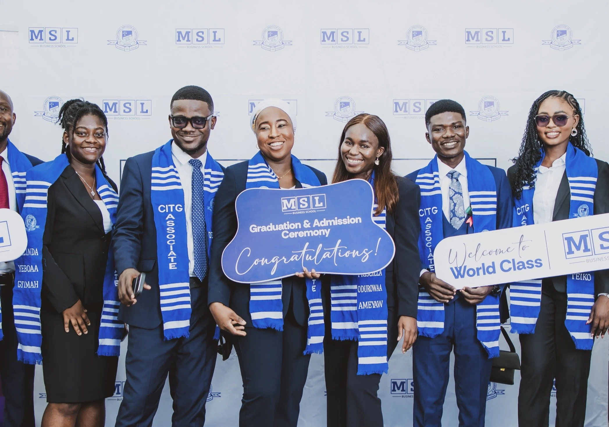 A group of MSL students celebrating with World Class and Congratulations placards in front of an MSL backdrop