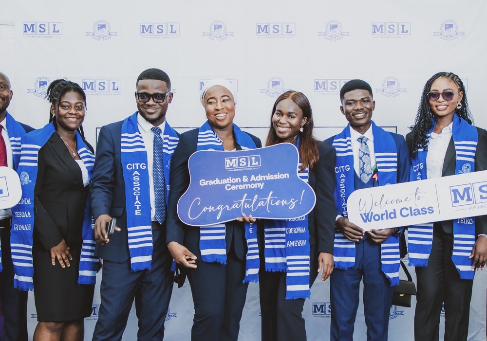 A group of MSL students celebrating with World Class and Congratulations placards in front of an MSL backdrop