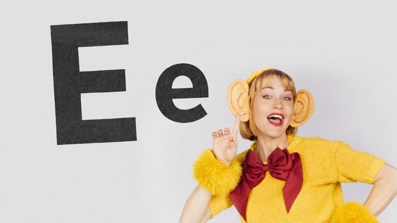 Word Playground performer in a yellow costume with oversized ears beside the letters Ee