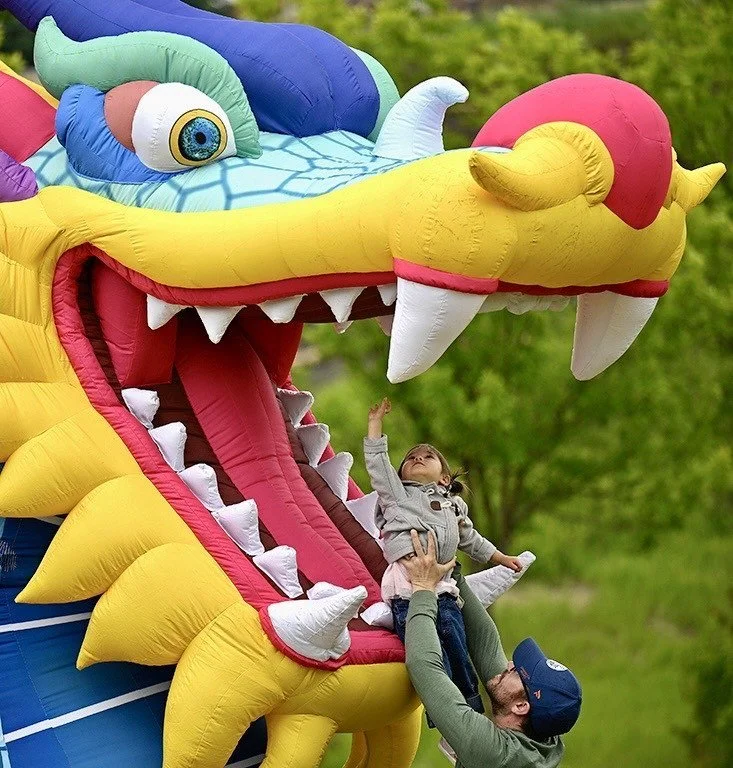 A parent lifts a small child up to a giant inflatable dragon