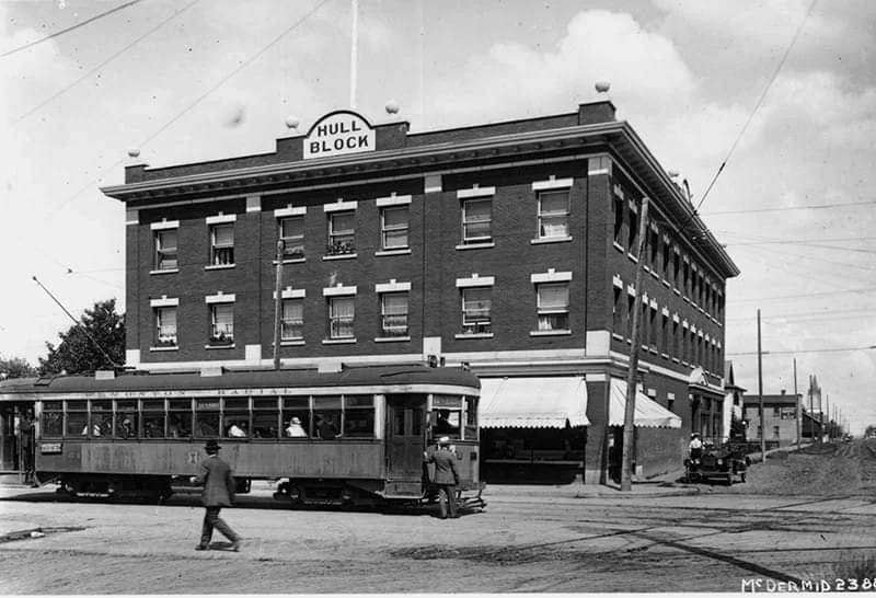 Historic photograph of the Hull Block, home of the CTC Storytelling Centre, with a streetcar passing in front, 1916
