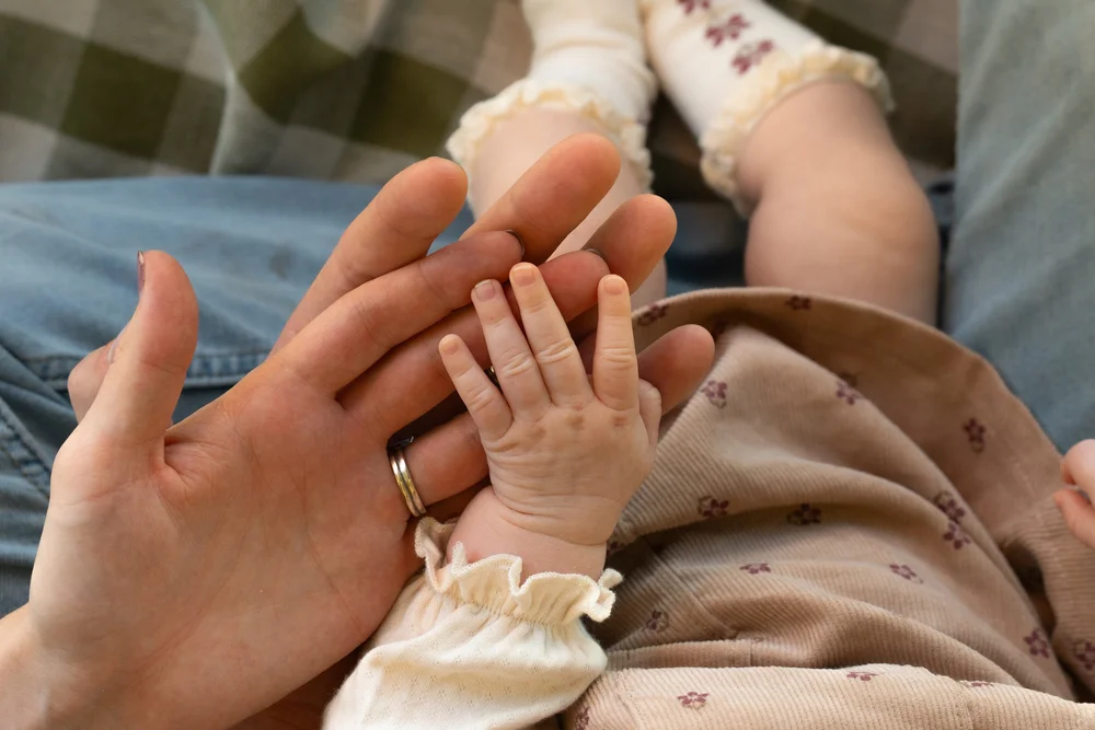 A baby’s hand resting against a parent’s hand.