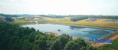 Wide aerial view of a manure lagoon with agitation equipment, surrounded by trees, farm buildings and Nebraska fields.