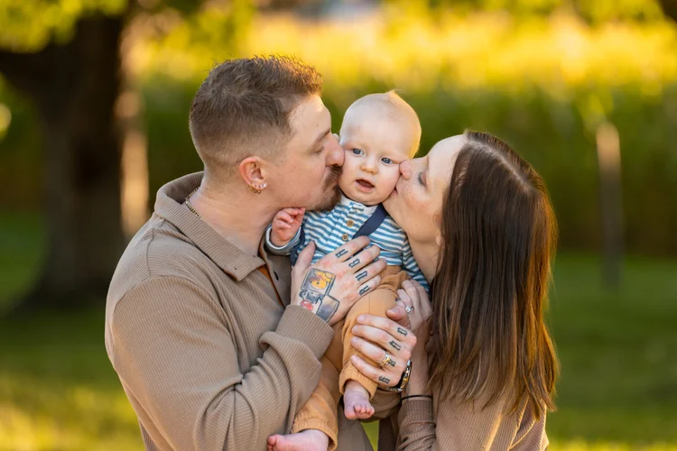 Parents kissing their baby’s cheeks during an outdoor fall mini session.