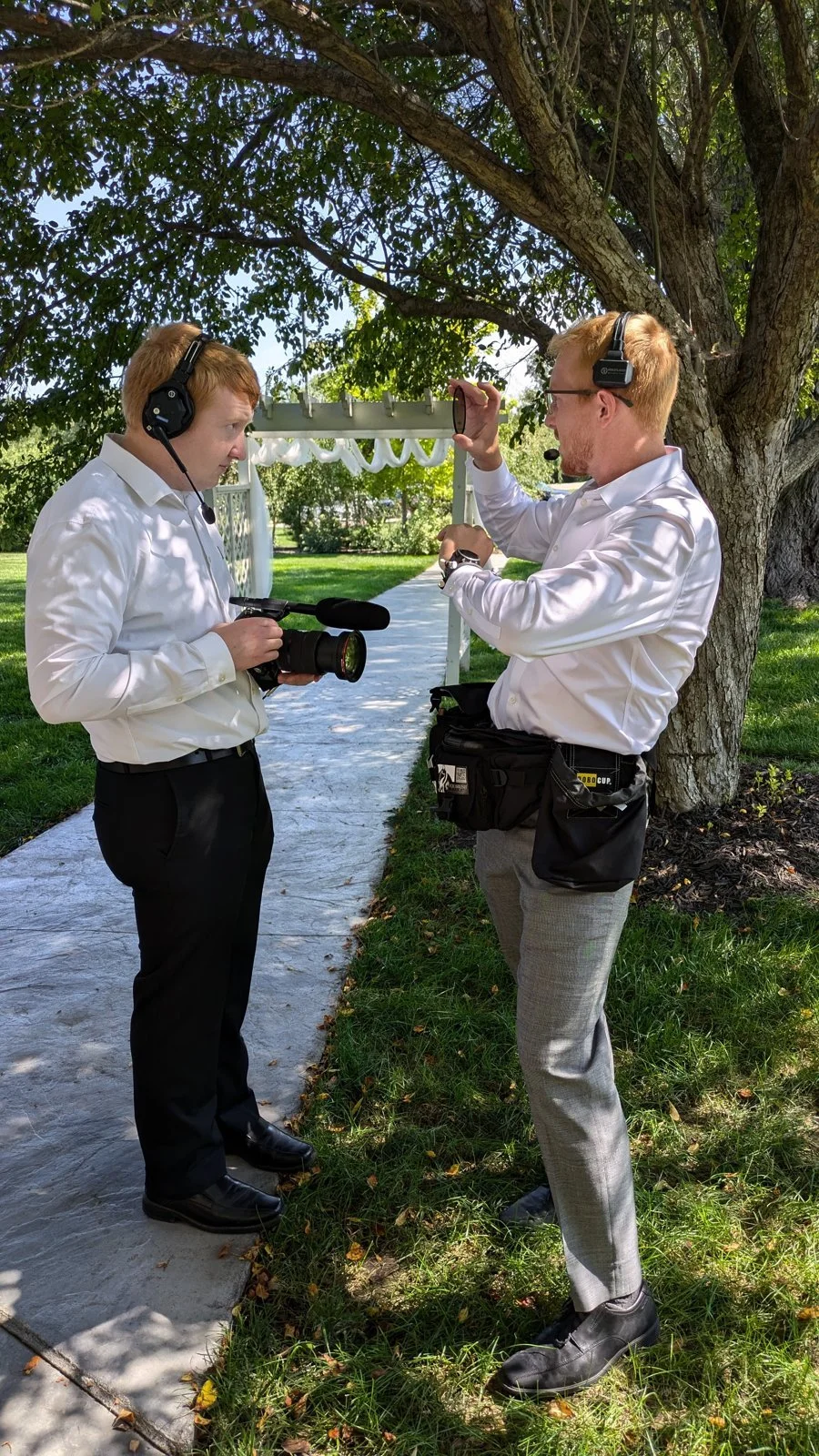 Two Fox Brush Films crew members wearing headsets and checking their cameras outdoors.