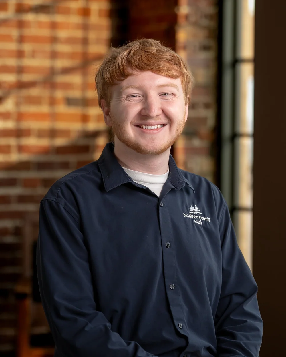 Trey smiling in his work polo beside a brick wall during a professional headshot session